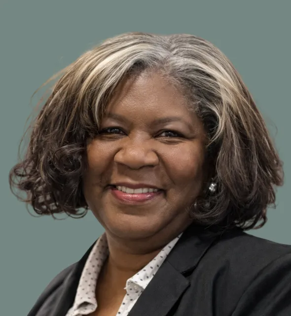 Portrait of a smiling Black woman with graying hair, wearing a black blazer and white polka dot shirt.