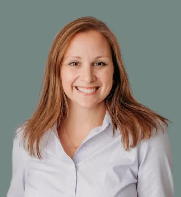 Portrait of a woman with auburn hair and a friendly smile, wearing a light blue collared shirt.