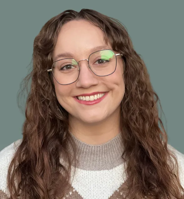 Portrait of a smiling woman with curly brown hair and glasses.