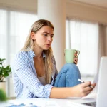 Woman with coffee reviews document near laptop, related to Title IX