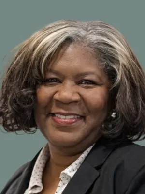 Portrait of a smiling Black woman with graying hair, wearing a black blazer and white polka dot shirt.